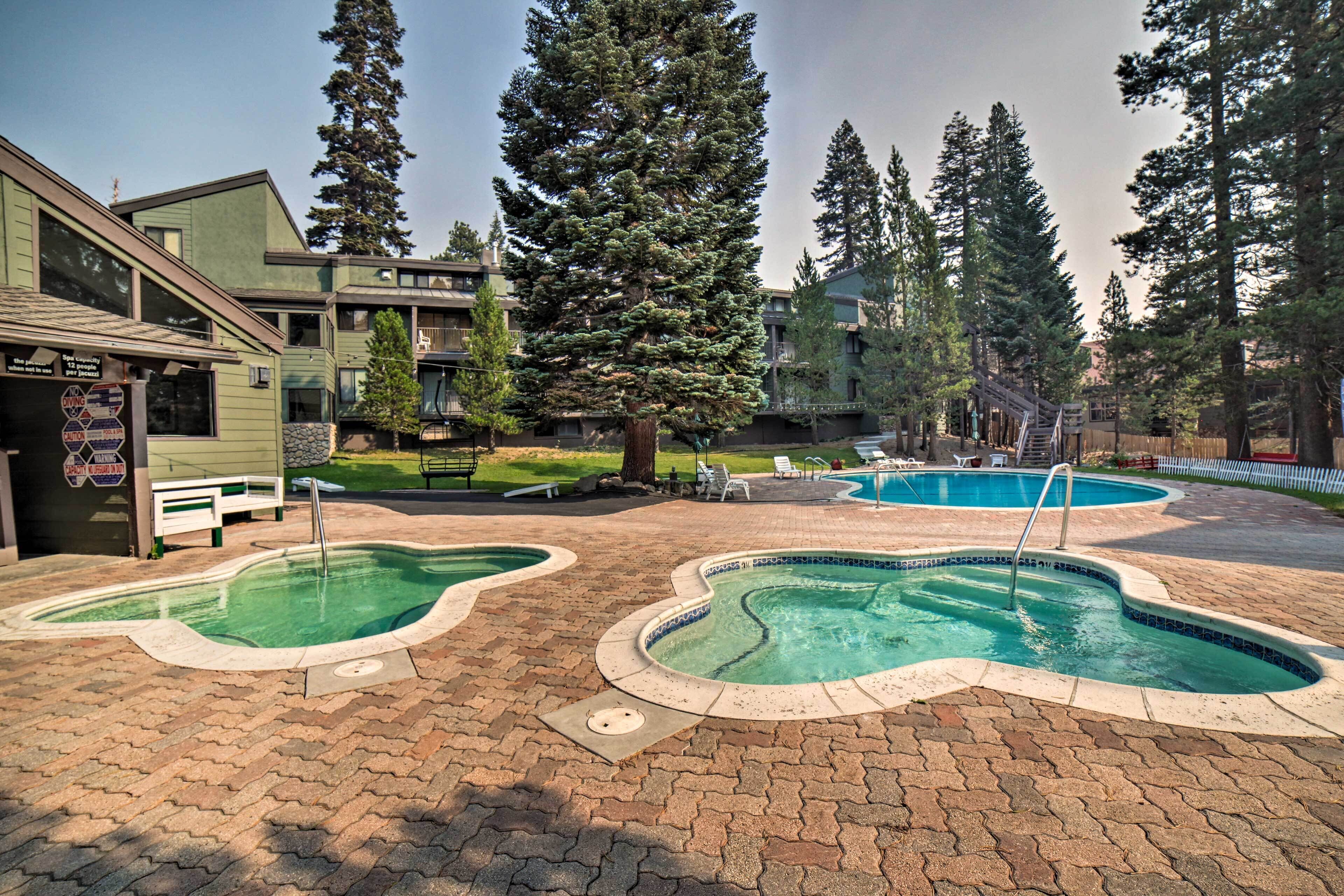 A pool area with two kidney-shaped pools, surrounded by a brick patio and a wooden deck.