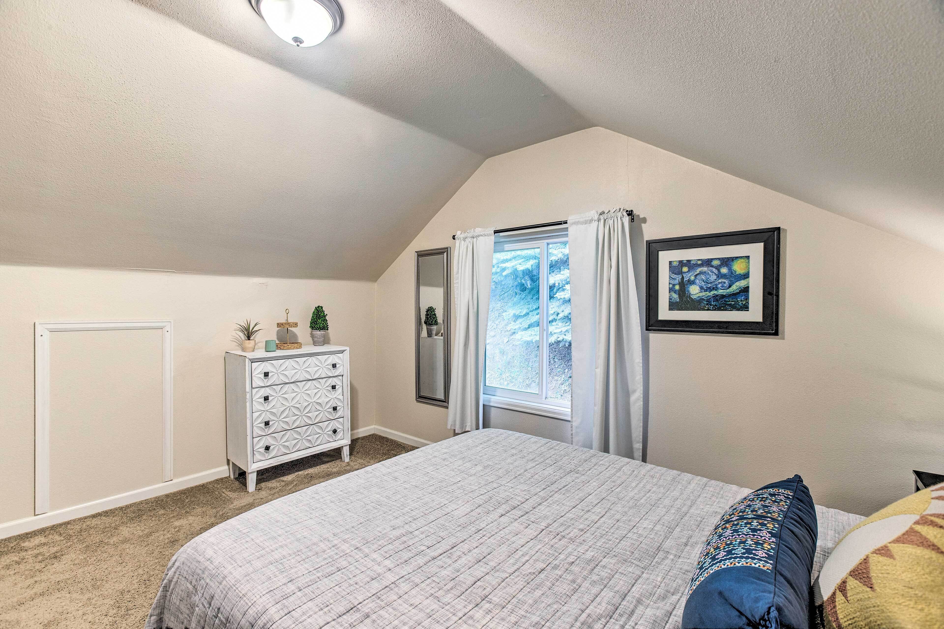 Une chambre à coucher avec un lit, une commode, une fenêtre avec des rideaux et un tableau encadré au mur.