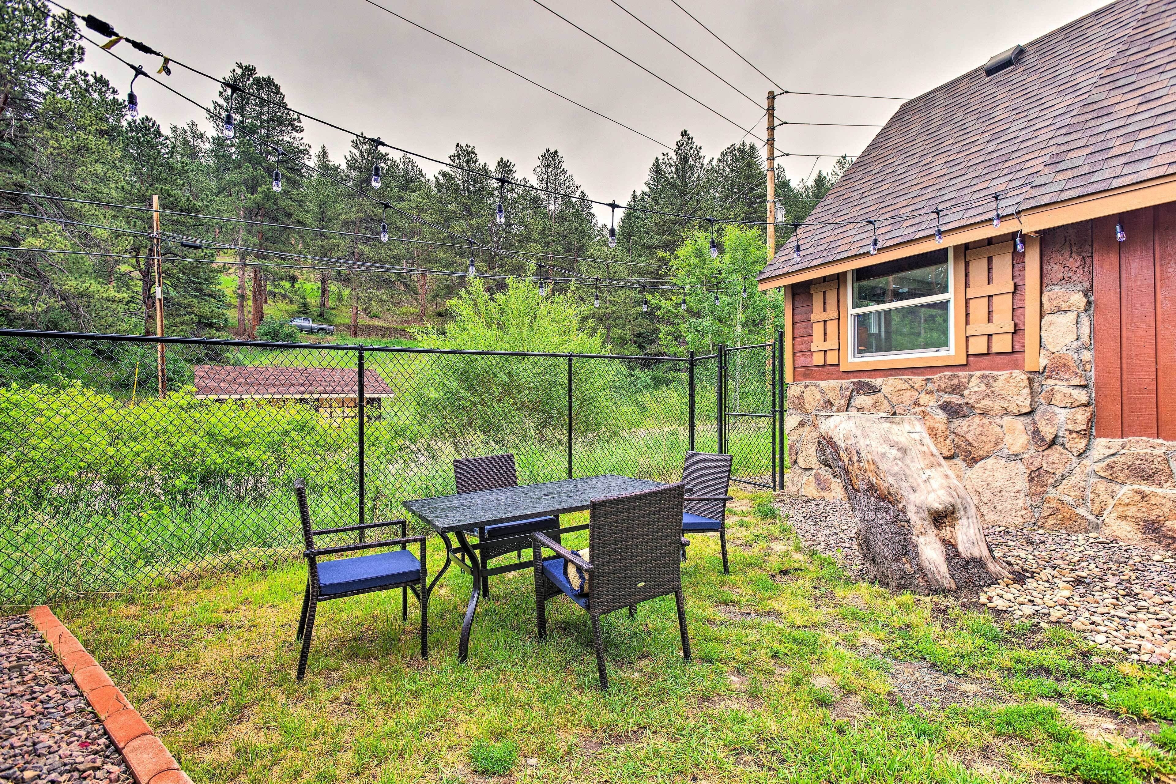 A fenced outdoor area with a table and chairs, a stone wall, and a house with a red roof.