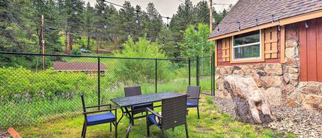 A fenced outdoor area with a table and chairs, a stone wall, and a house with a red roof.