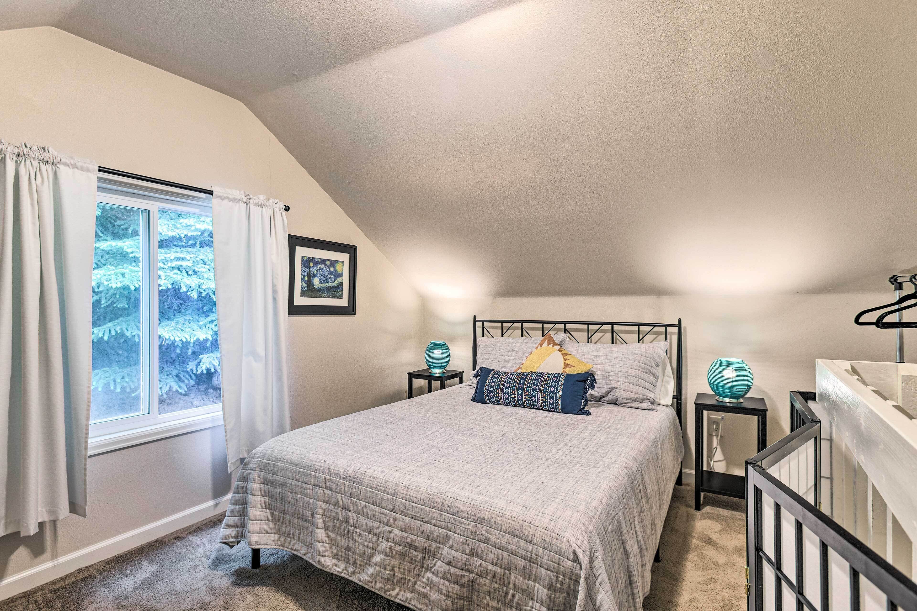 A bedroom with a bed, a window with curtains, a bedside table with a lamp, and a picture on the wall.
