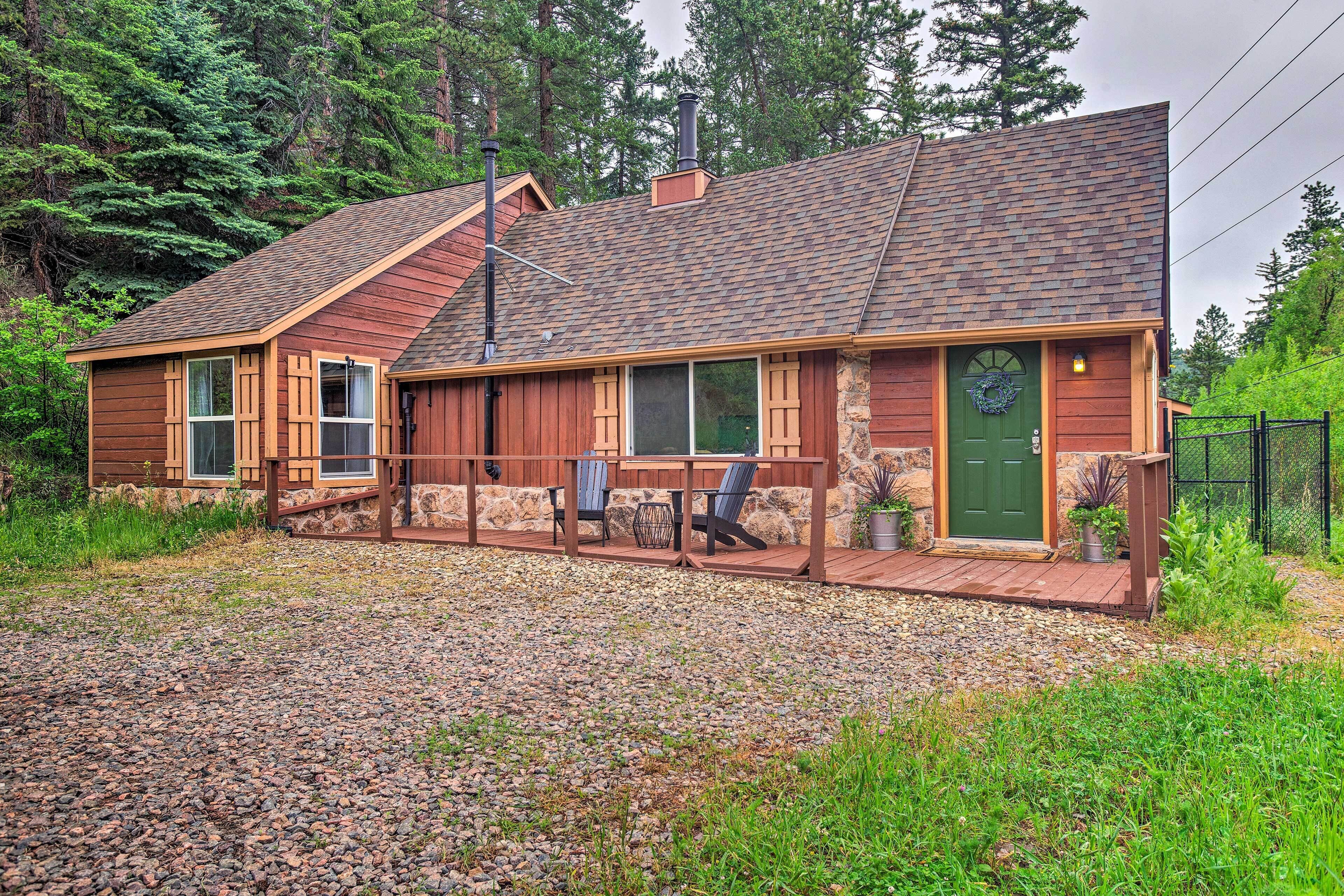 A wooden cabin with a stone foundation, a wooden deck, and a green door.