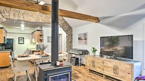 A cozy living room with a stone arch, a fireplace, a television, and wooden cabinets. - Creekside Morrison Cabin ~ 9 Mi to Red Rocks Park! (Morrison)