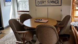 Un coin repas avec une table ronde, quatre chaises et un tapis. Une affiche sur le mur porte l’inscription : « CHAQUE ÉTÉ A SON HISTOIRE ».