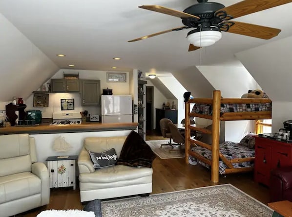 A loft-style room with a kitchen, a bunk bed, a sofa, and a ceiling fan. - Cottage on Munro Lake (Levering)