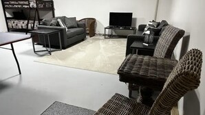 Un salon moderne avec un canapé gris, une table basse noire, un fauteuil en osier et un téléviseur posé sur un meuble.