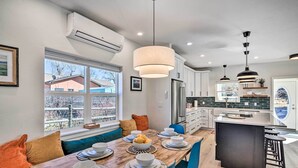 A modern kitchen with a central island, dining area with a long table set for four, and a view of the outside through large windows. - Charming Buena Vista Home w/ Private Hot Tub! (Buena Vista)