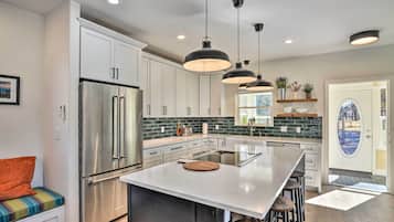 A modern kitchen with stainless steel appliances, a large island, pendant lighting, and a view through a glass door.