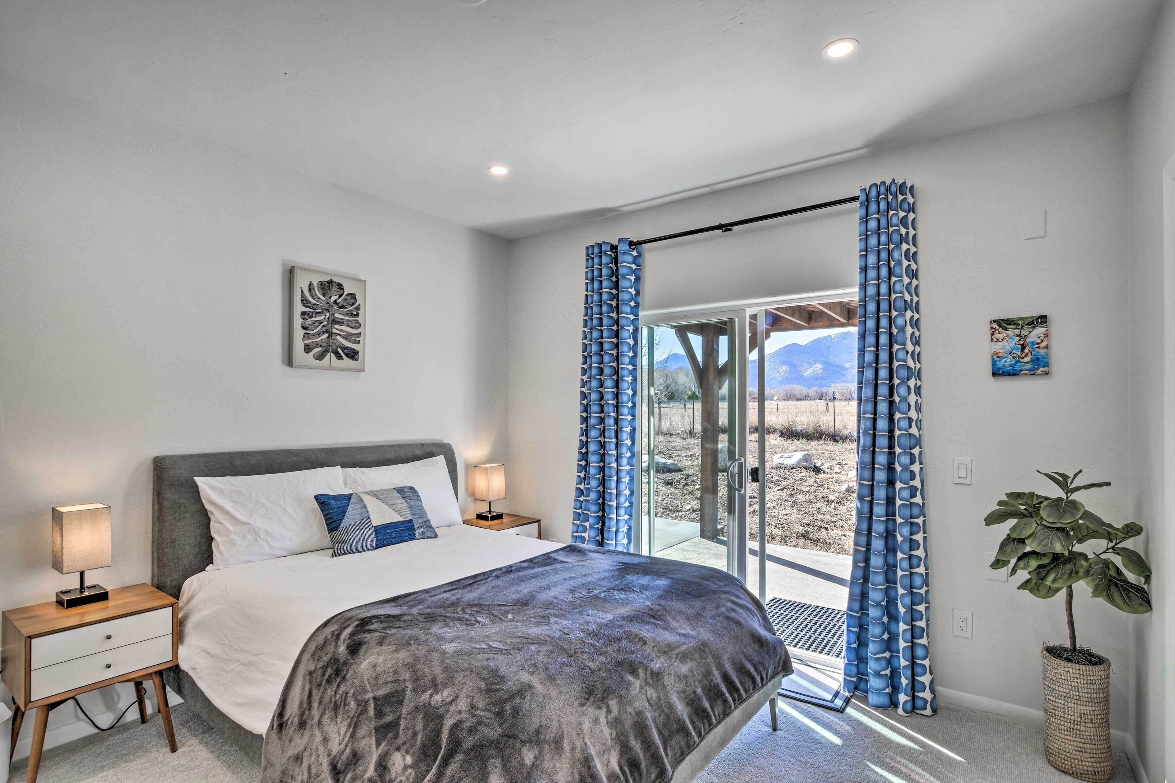 A bedroom with a bed, nightstands, a potted plant, and a view through a glass door.