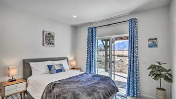 A bedroom with a bed, nightstands, a potted plant, and a view through a glass door.
