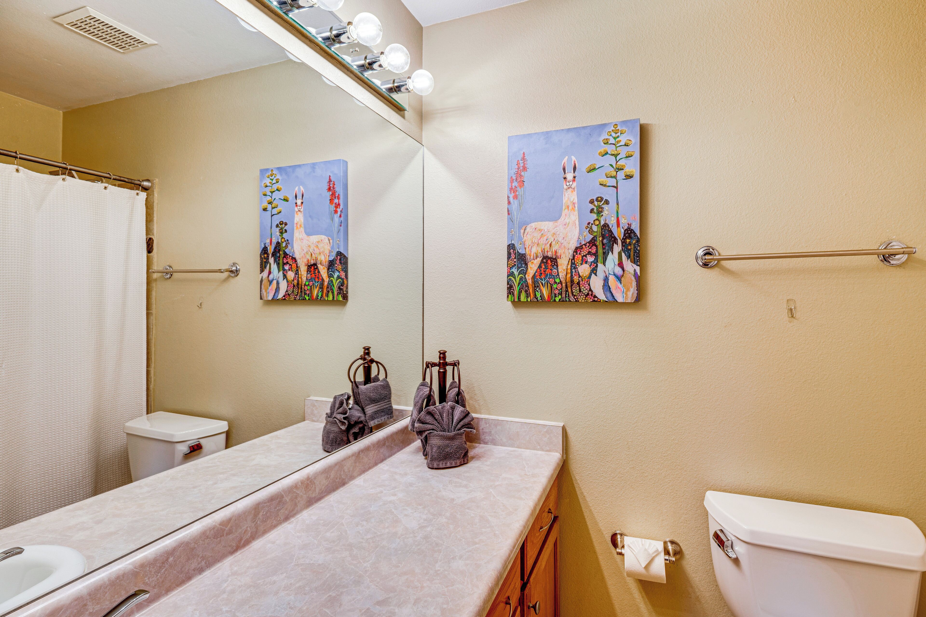 Ein Badezimmer mit Waschbecken, Spiegel, Handtuchhalter, Toilette und zwei Bildern an der Wand.