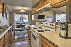 A modern kitchen with wooden cabinets, a white stove, a coffee maker, and a dining area with a bench. - Manitou Springs Escape w/ A/C & Private Deck! (Manitou Springs)