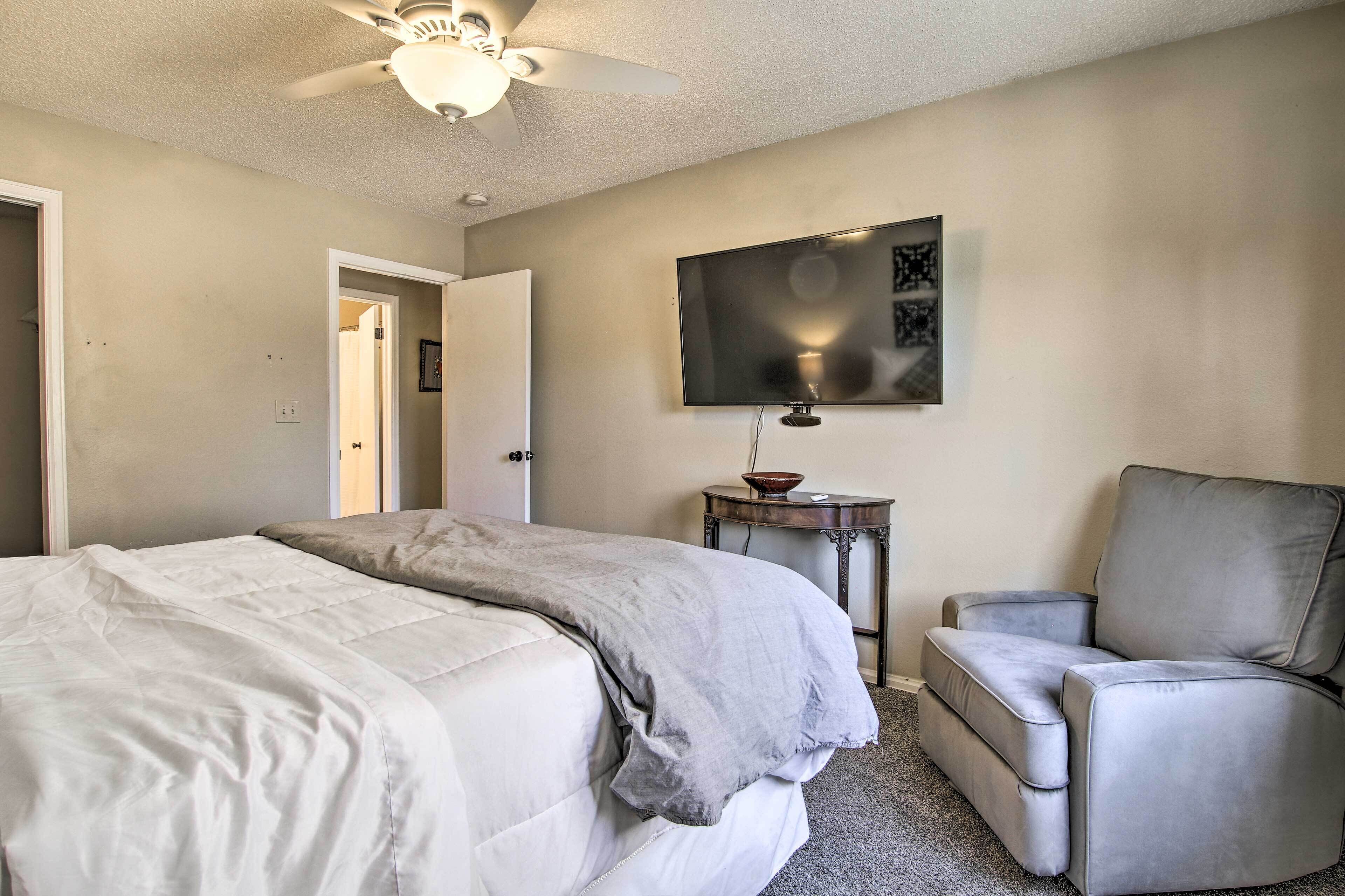 A bedroom with a bed, a chair, a television on the wall, and a ceiling fan.