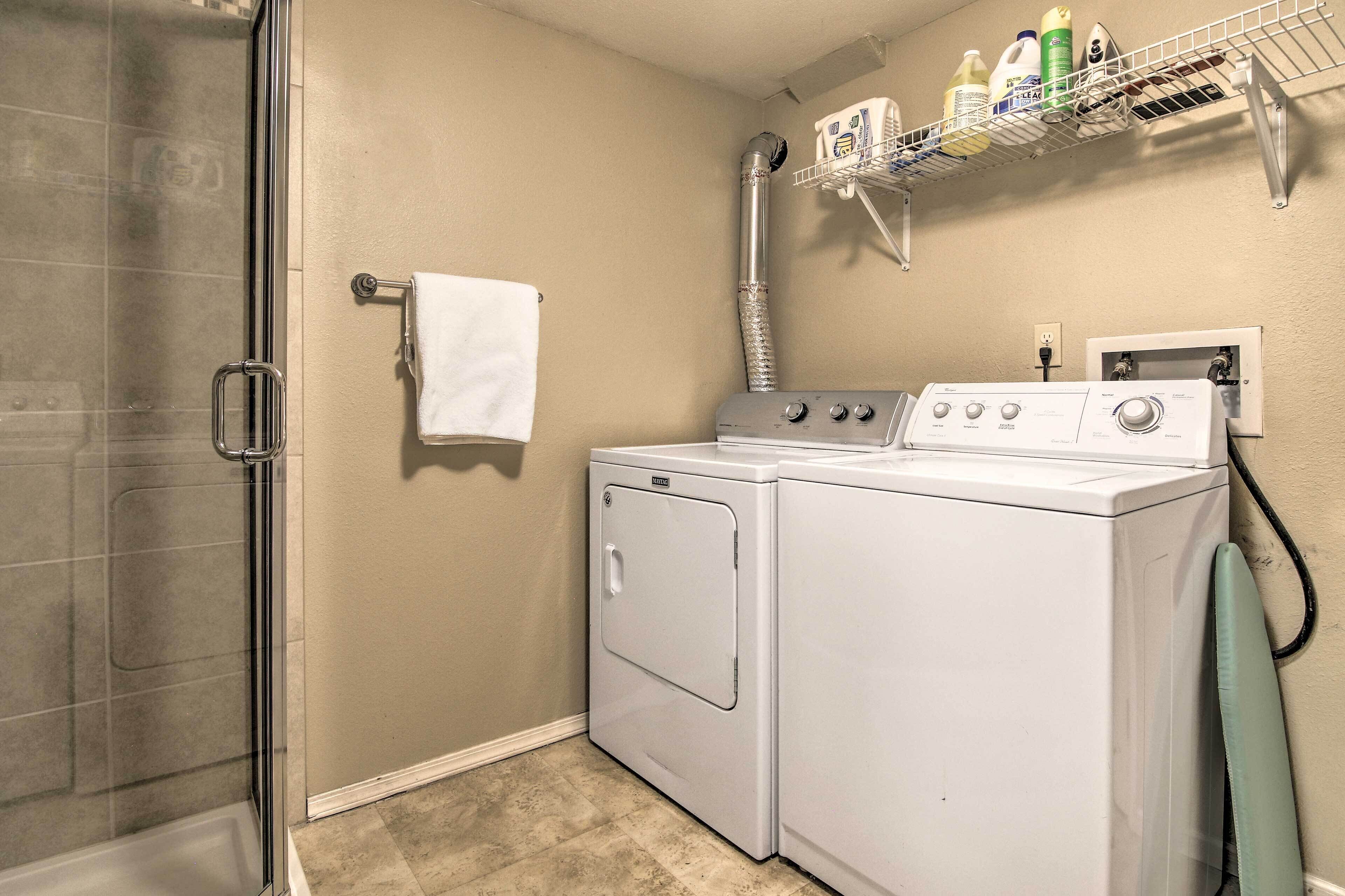 Un cuarto de lavandería con lavadora, secadora y un estante metálico superior con productos de limpieza.