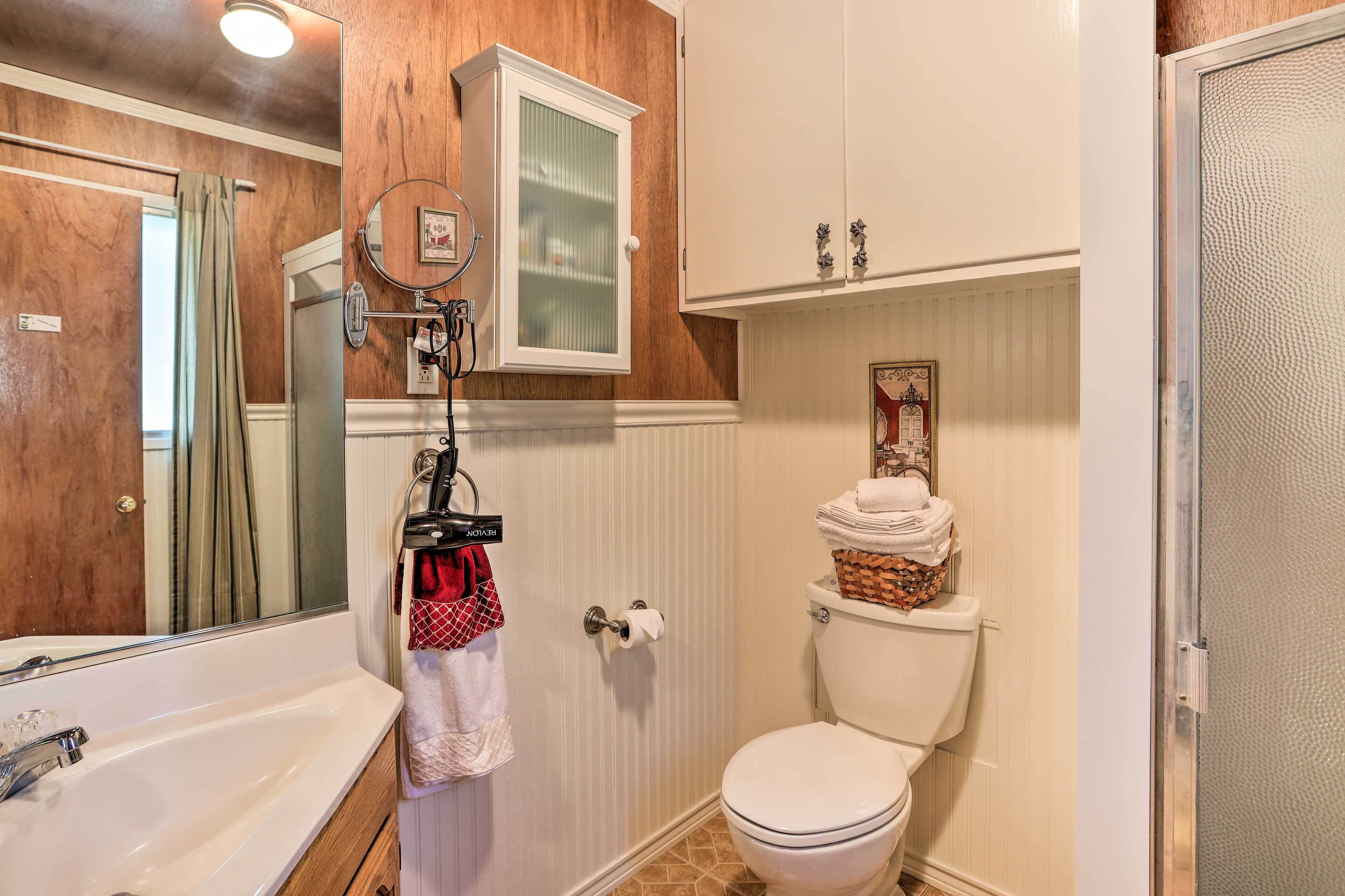 Un baño con pared de paneles de madera, inodoro y lavamanos blancos, y cabina de ducha.