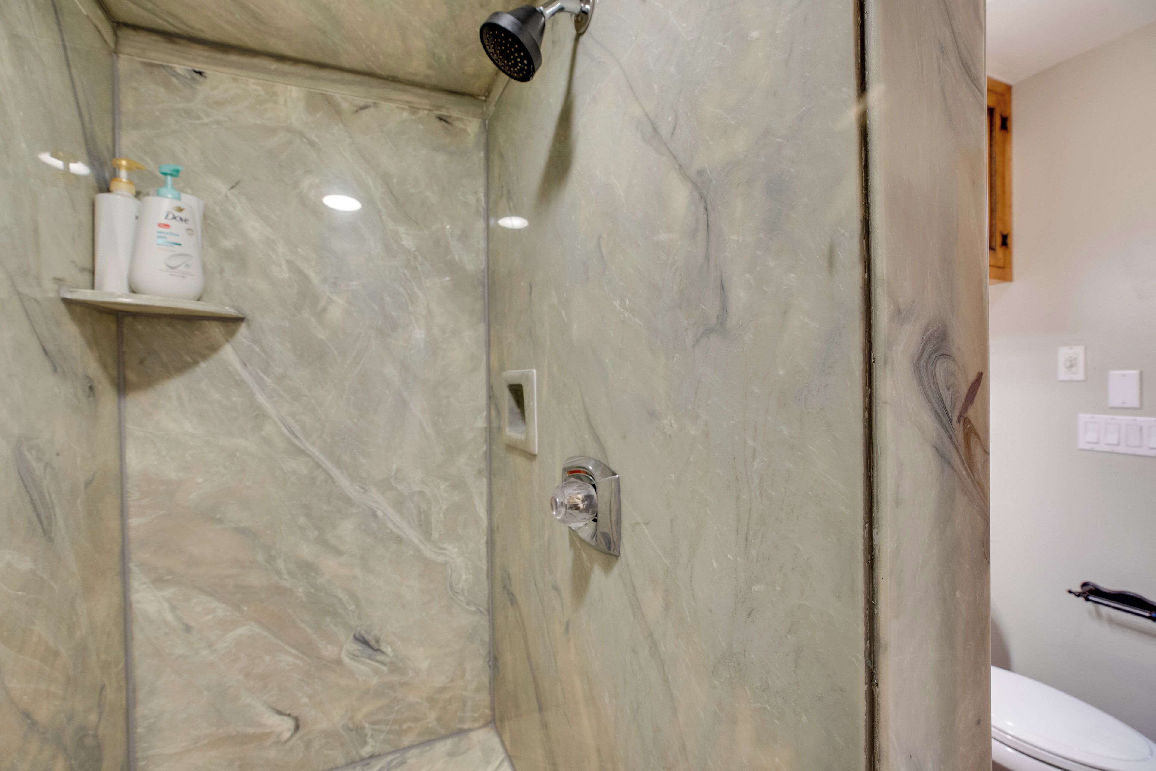 Une salle de bain avec une douche, des murs en marbre et des toilettes.