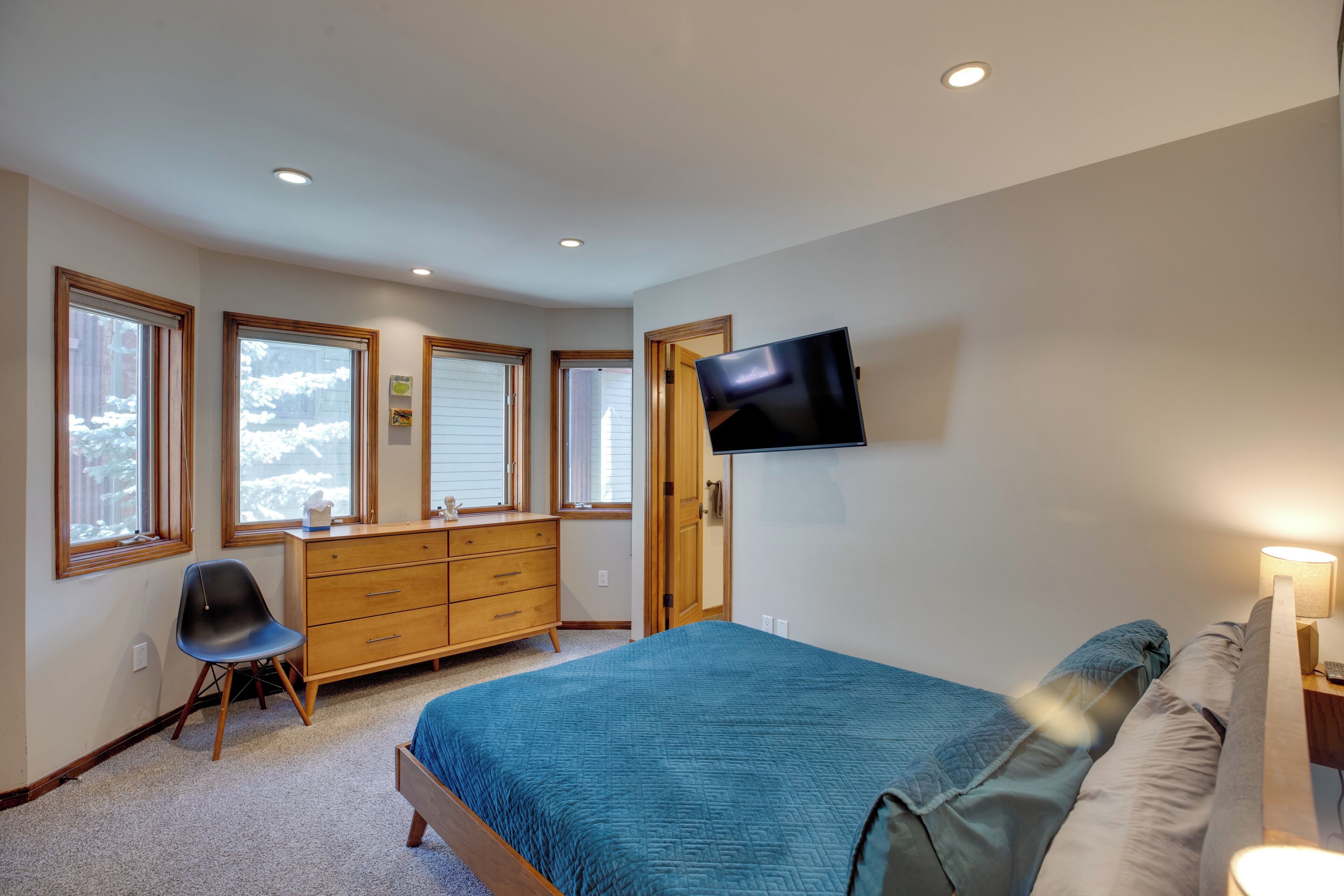 Un dormitorio con cama, cómoda, silla y televisión montada en la pared.