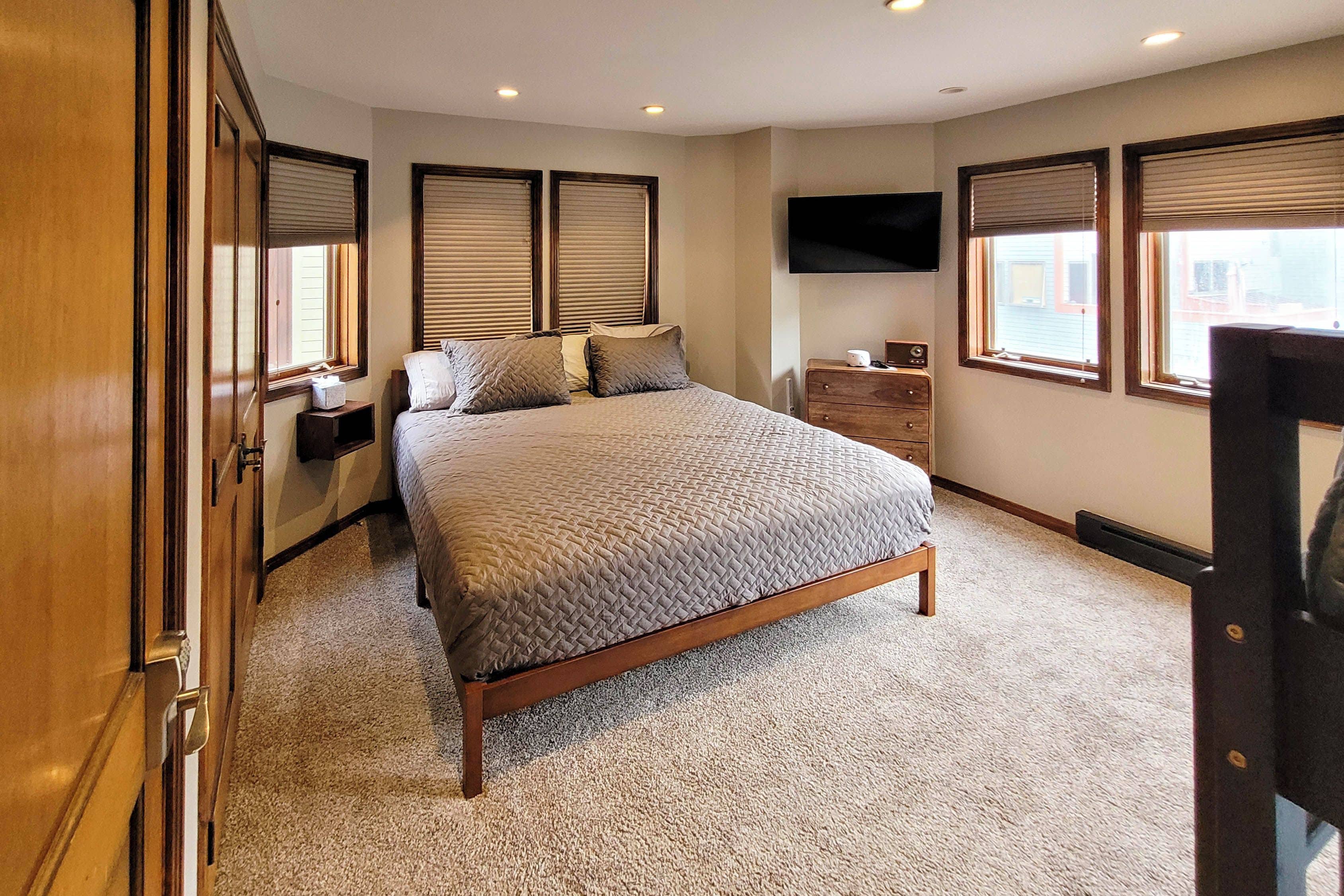 Quarto com cama, cômoda, TV e janelas.