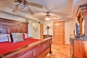 A bedroom with a large wooden bed, two ceiling fans, wooden doors, a dresser, and a television. - 40-acre Farm w/ Animals & Fishing in Sebring! (Sebring)
