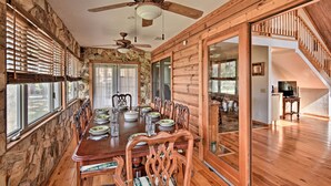 A dining area with a wooden table set for six, flanked by stone walls and large windows.