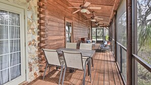 A wooden deck with a table and chairs, ceiling fans, and a view of trees.