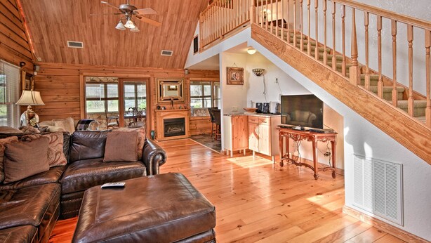 A spacious living room with a large brown leather sofa, a fireplace, and a wooden staircase. - 40-acre Farm w/ Animals & Fishing in Sebring! (Sebring)