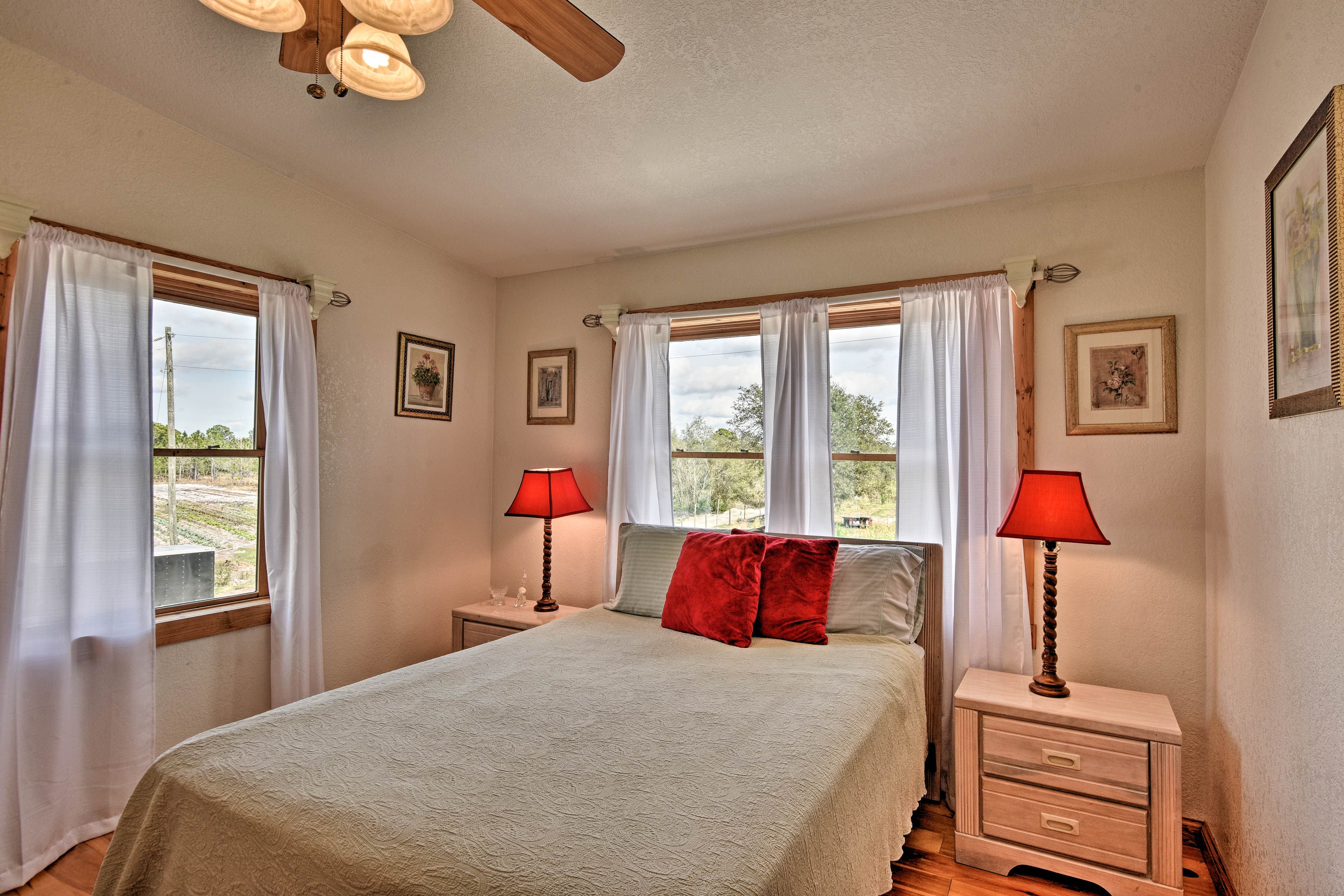 A bedroom with a bed, two nightstands with lamps, a ceiling fan, and windows with curtains.