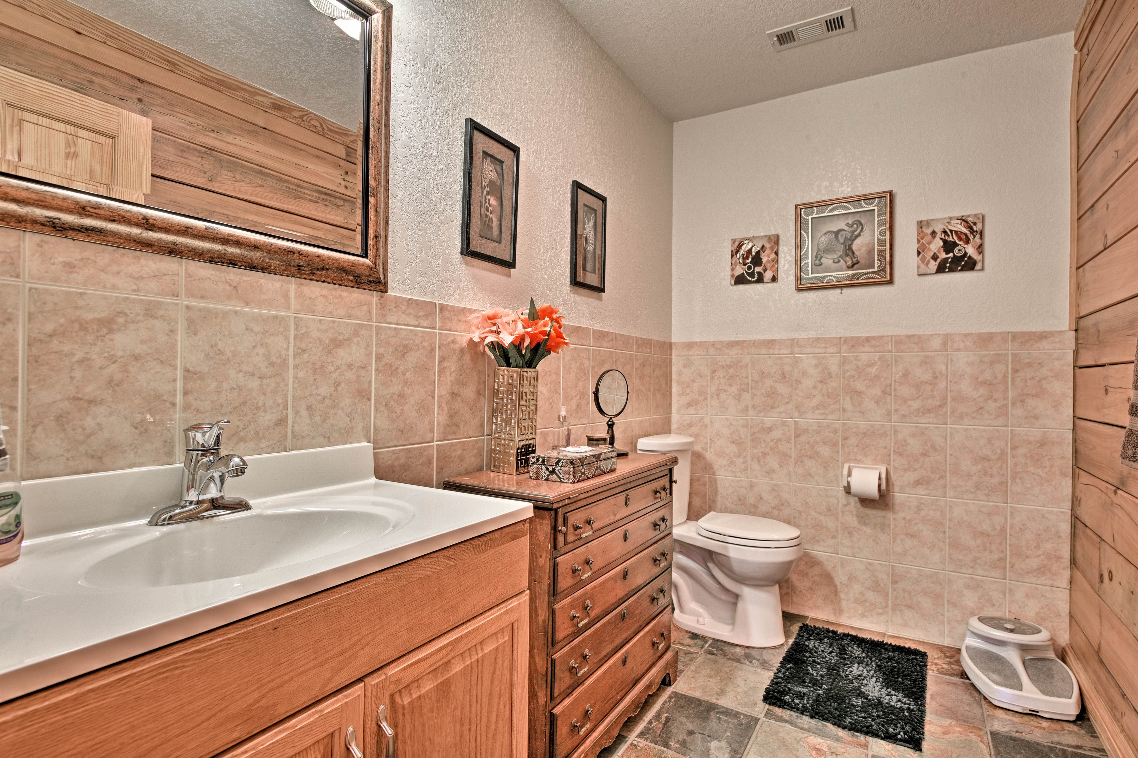 A bathroom with a wooden vanity, a sink, a toilet, and a mirror. There are three framed pictures on the wall.