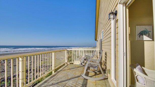 A balcony with a view of the ocean, a rocking chair, and a wicker chair. - Quiet Waterfront Escape w/ Hot Tub & Beach Access! (Gold Beach)
