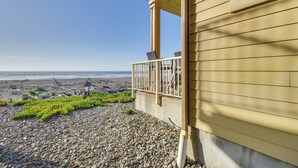 A building with a balcony overlooking a rocky beach with sparse vegetation. - Quiet Waterfront Escape w/ Hot Tub & Beach Access! (Gold Beach)