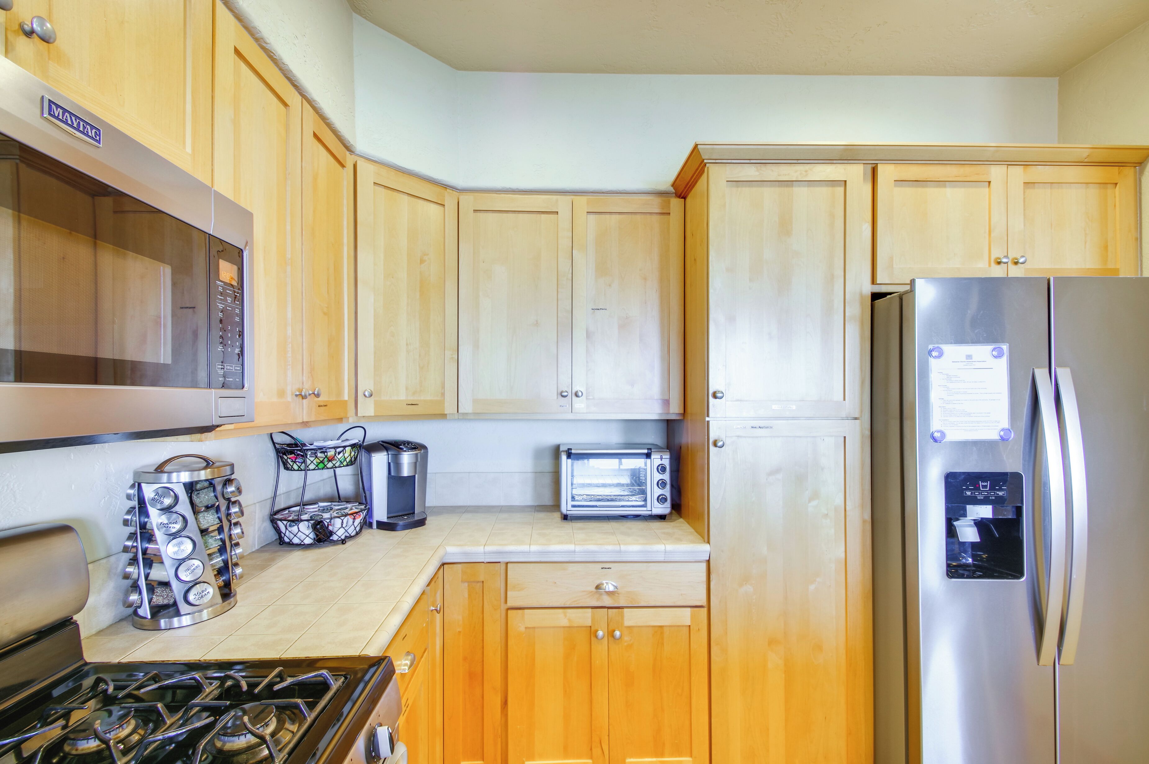 A kitchen with wooden cabinets, a stainless steel refrigerator, a stove, a microwave, a toaster, and a coffee maker.