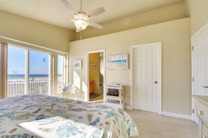 A bedroom with a bed, a ceiling fan, a door, and a view of the beach.