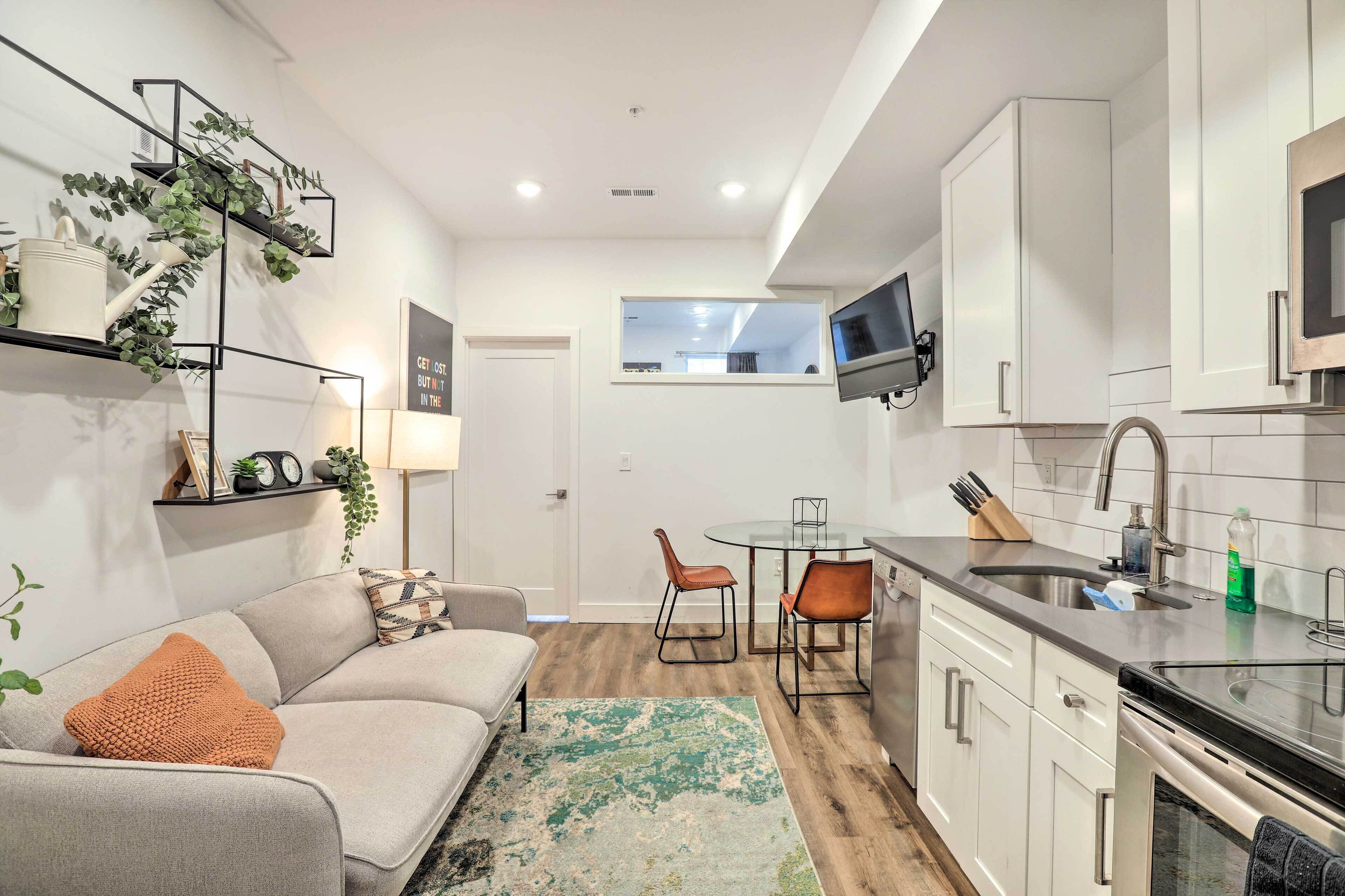 A compact living space with a kitchenette, a sofa with a throw pillow, a dining table with chairs, and a window overlooking the interior.