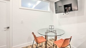 A room with a round glass table, two leather chairs, a mounted TV, and a window with a view of the sky. - Classy Philly Apartment: 2 Mi to Downtown! (Philadelphia)