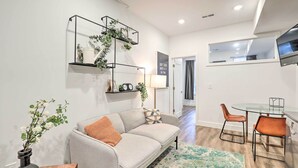 A modern living room with a sofa, coffee table, and chairs, a TV mounted on the wall, and a small plant on a shelf. - Classy Philly Apartment: 2 Mi to Downtown! (Philadelphia)