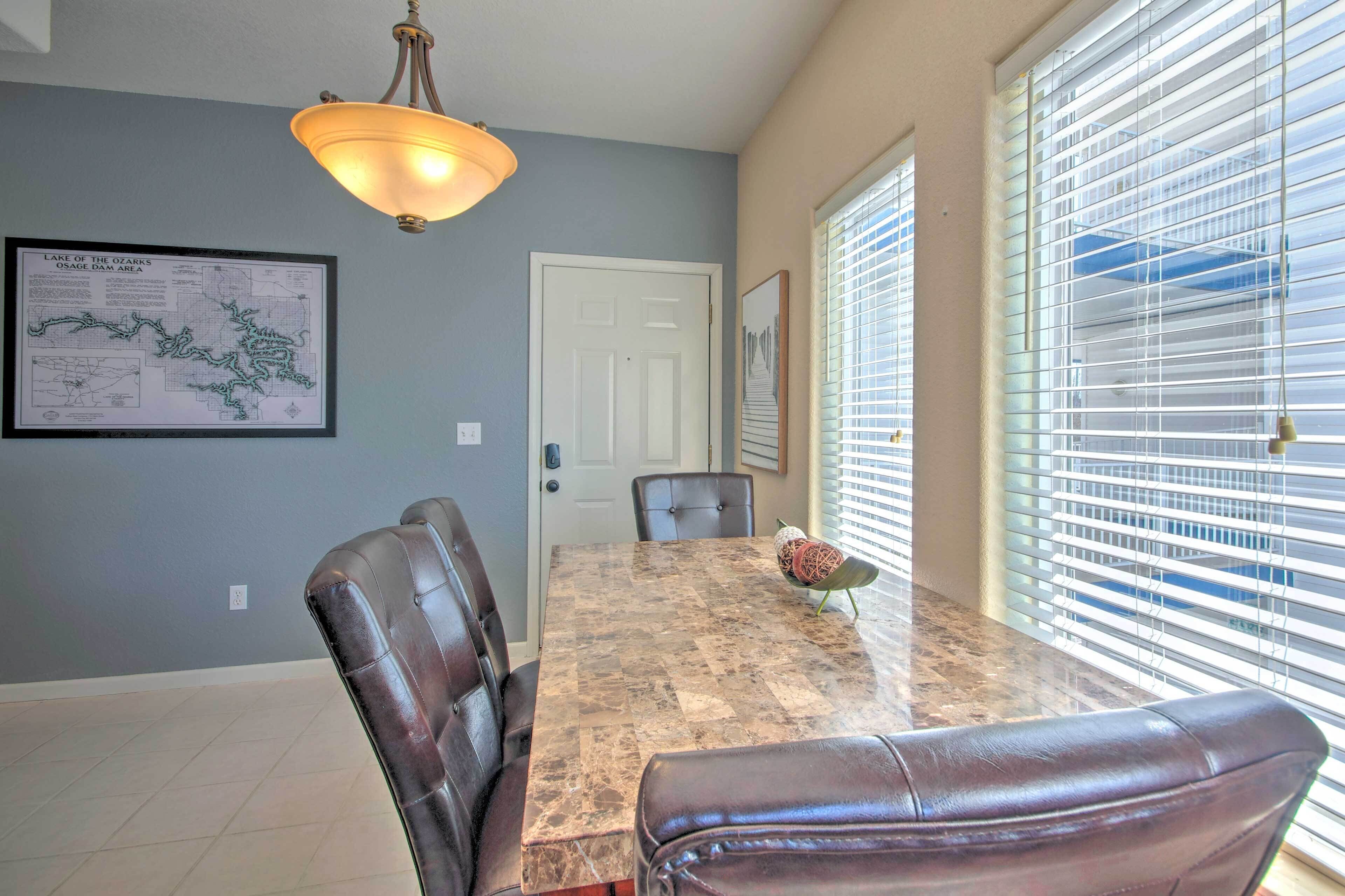 A dining area with a marble table, leather chairs, a chandelier, and a map on the wall.