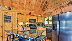 A modern kitchen with wooden cabinetry, a central island with bar stools, stainless steel appliances, and a chalkboard with a list of family values. - Cabin w/ BBQ + Games - Walk to Blue Ridge Parkway! (Sylva)