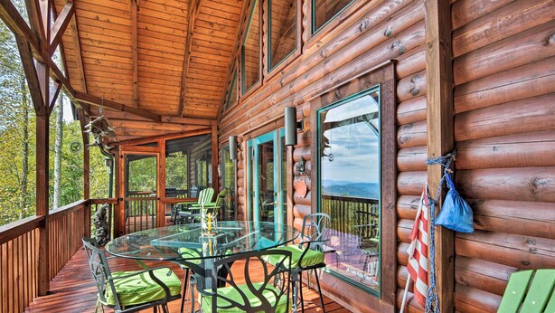 A wooden cabin with a glass dining table and chairs, a deck, and a view of the surrounding forest. - Cabin w/ BBQ + Games - Walk to Blue Ridge Parkway! (Sylva)