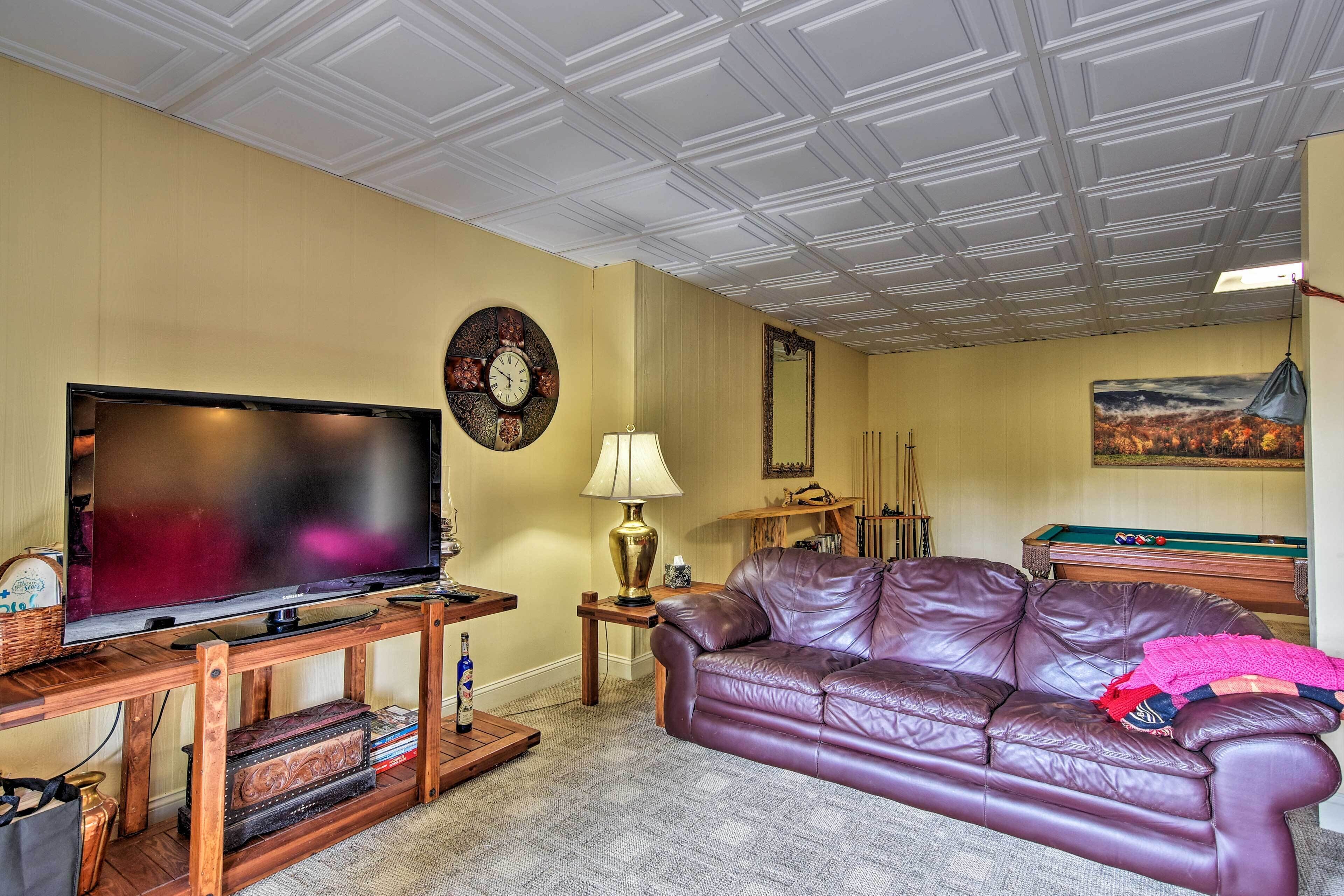 A living room with a television, leather sofa, wooden coffee table, and a pool table.