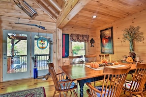 A wooden dining room with a large table and chairs, a decorative wall hanging, and a window with a view of the outdoors. - Cabin w/ BBQ + Games - Walk to Blue Ridge Parkway! (Sylva)