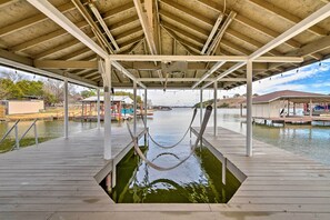 Ein überdachter Steg mit Hängematte, Holzterrasse und Wasser im Vordergrund.