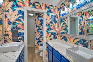 Ein Badezimmer mit farbenfroher Blumenfliesen als Rückwand, einem weißen Waschbecken und einem Spiegel darüber.