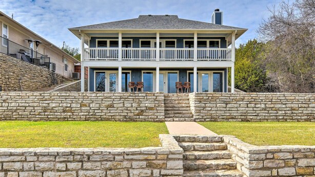 Une maison à deux étages, dotée d’un mur de soutènement en pierre et d’un balcon.