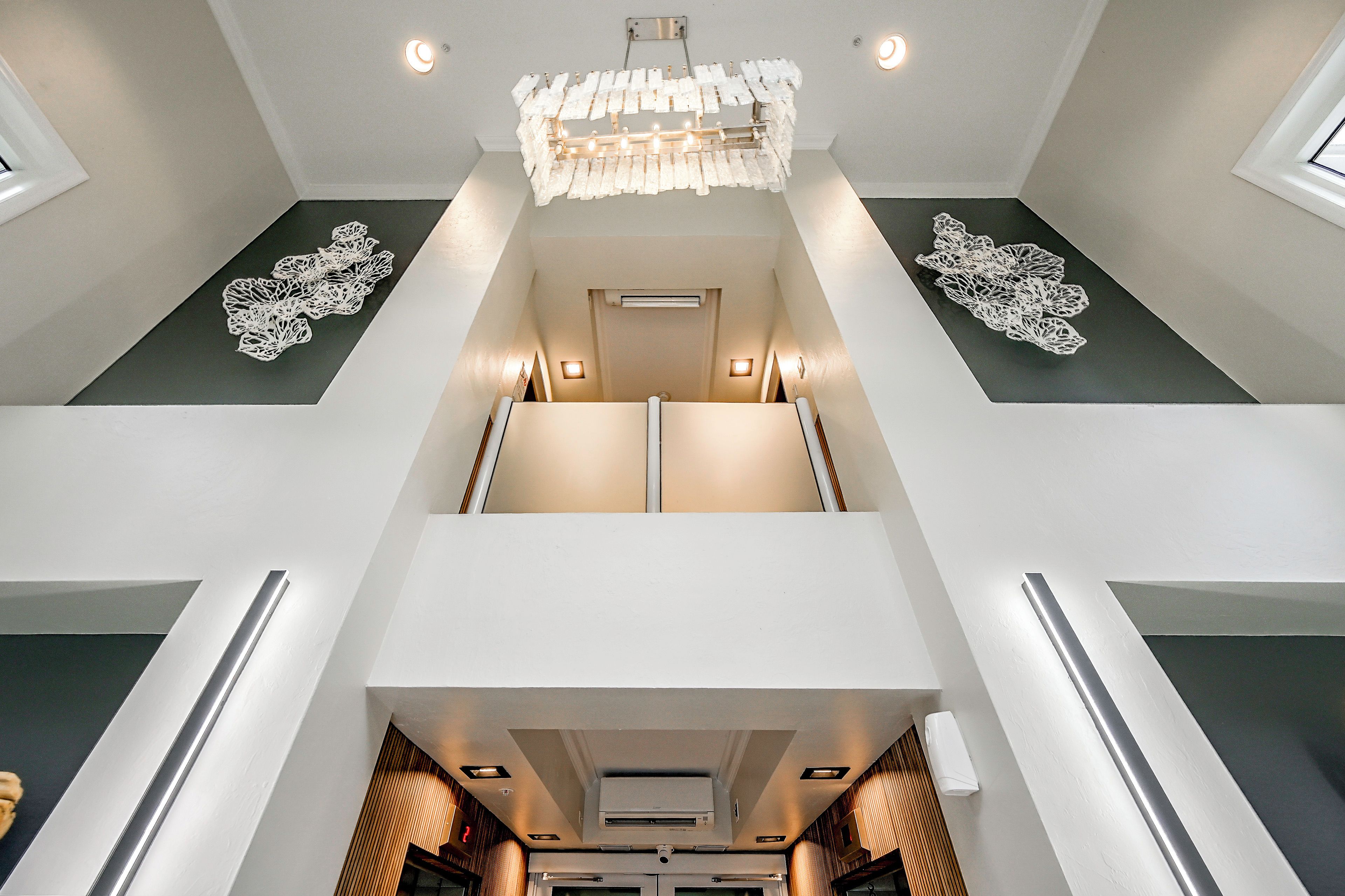 A modern hotel interior with a central staircase, a chandelier, and decorative wall art.
