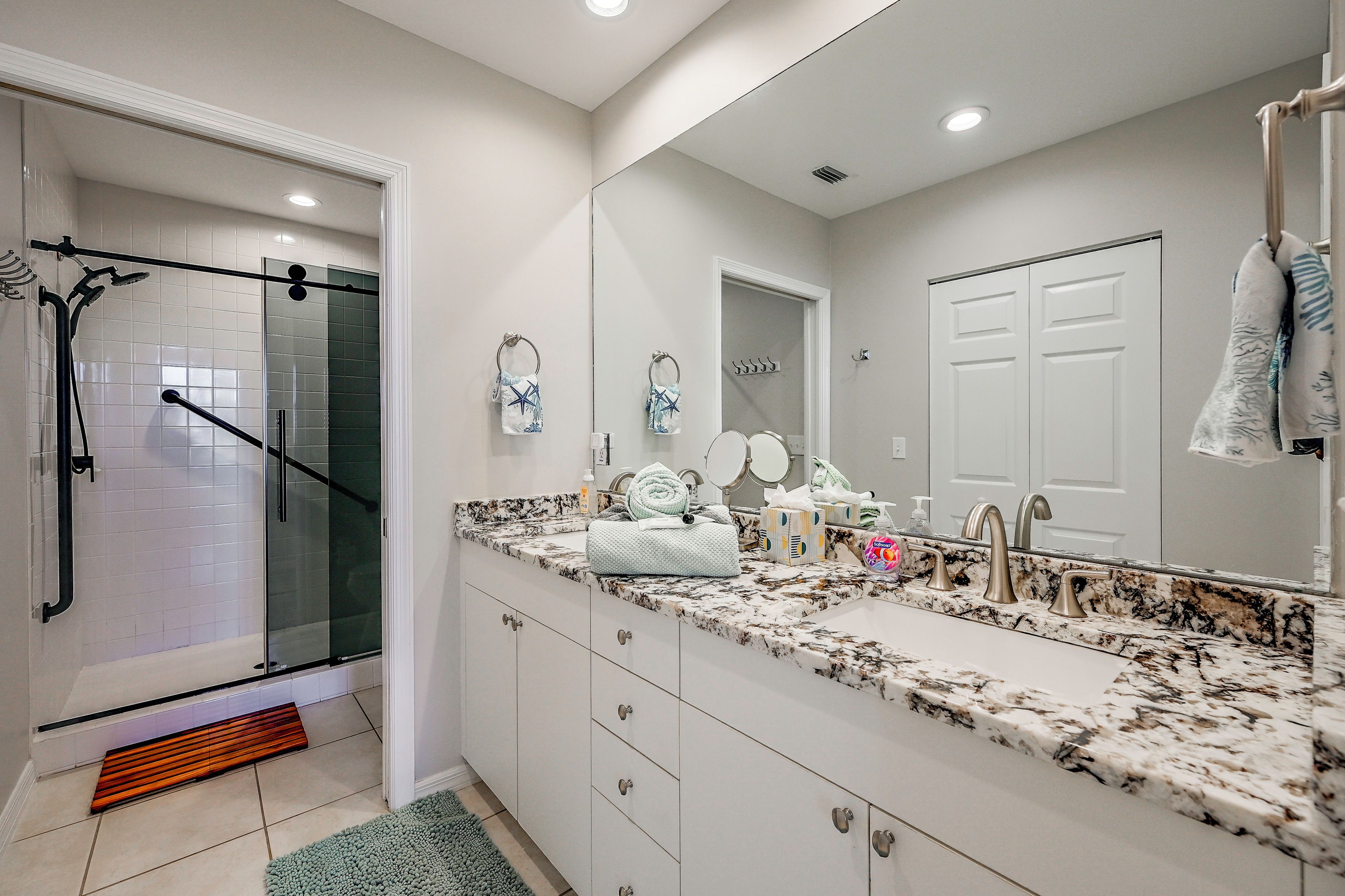 A modern bathroom with a glass shower enclosure, a marble countertop, and a large mirror.