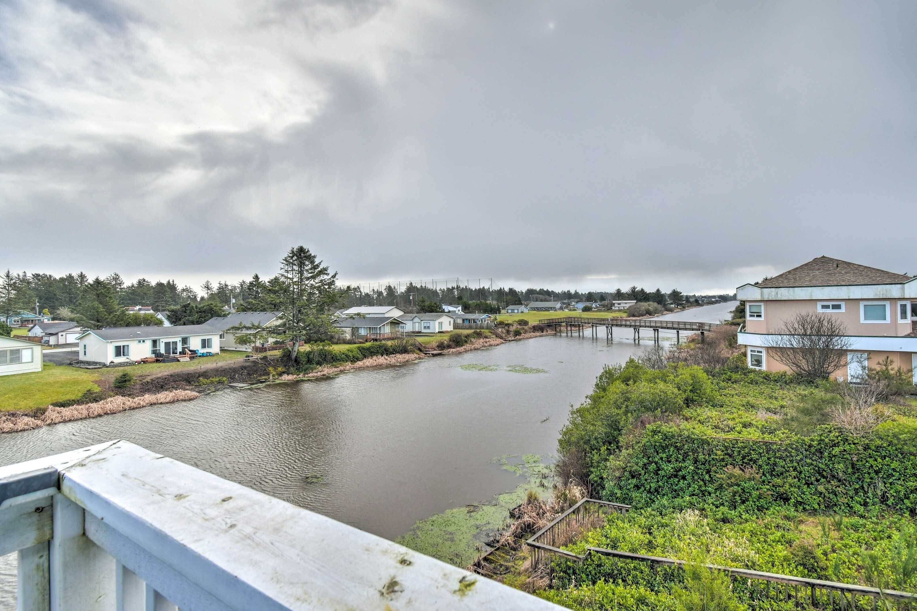 Un barrio residencial con casas a lo largo de un río, un puente de madera y una orilla cubierta de césped.
