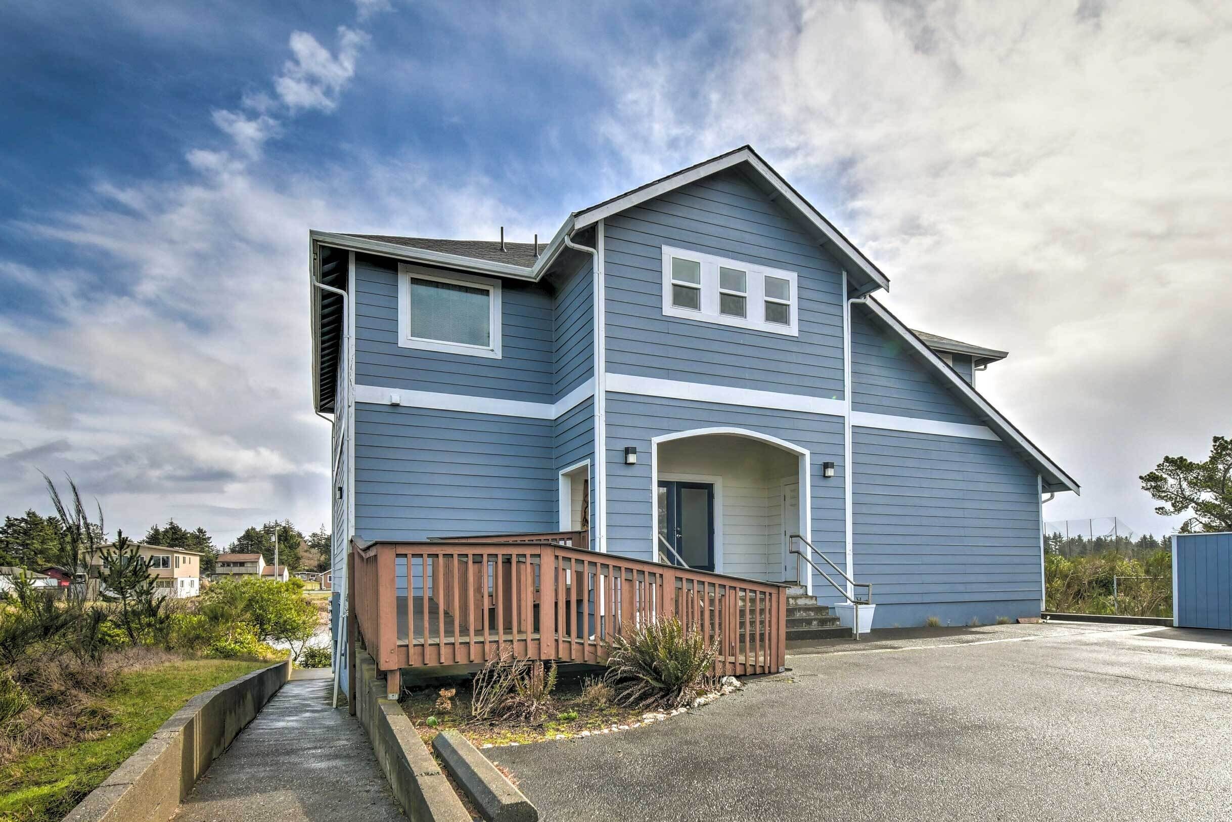 A two-story residential building with a blue exterior, a wooden deck, and a driveway.