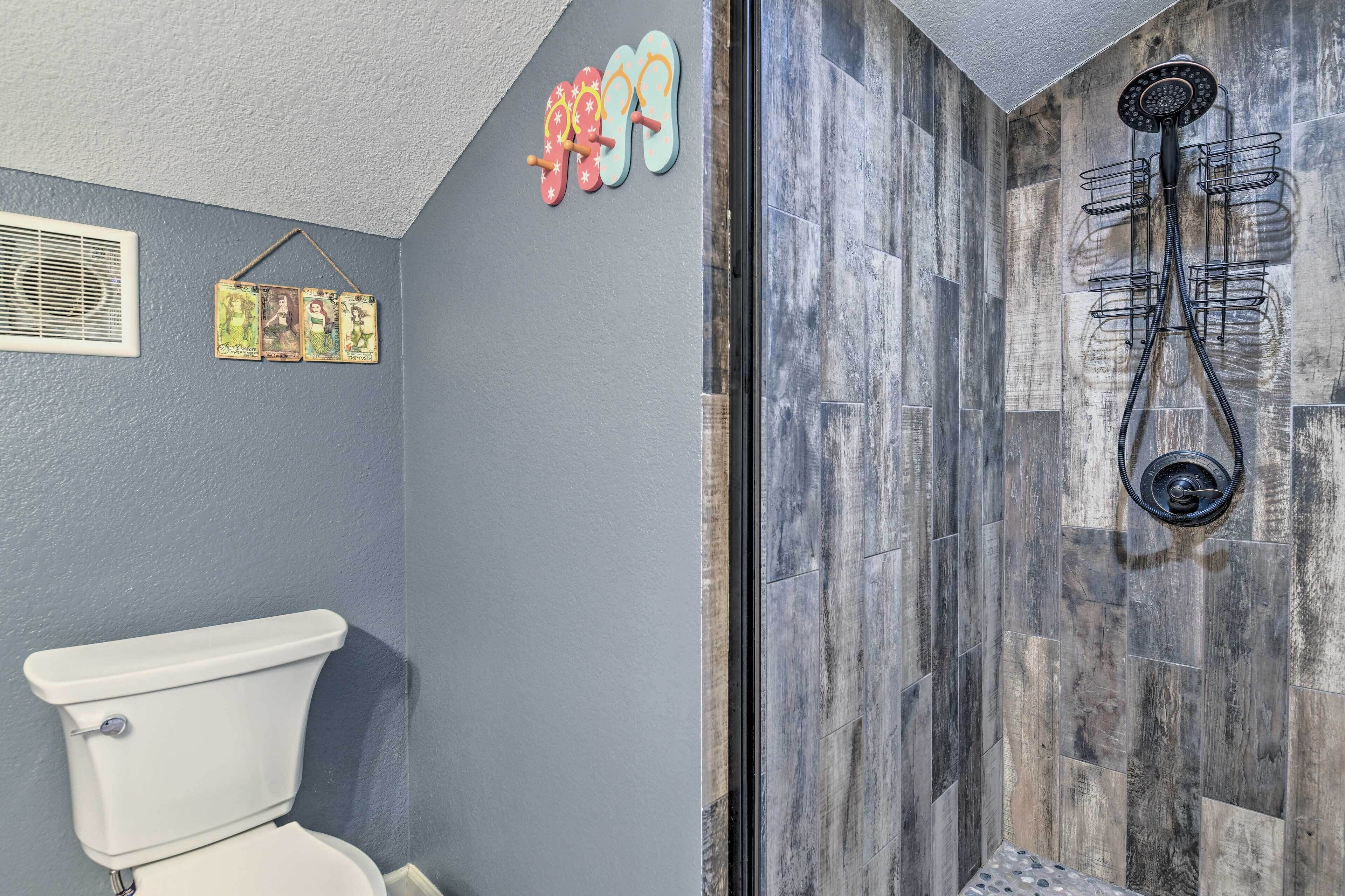 A bathroom with a toilet, shower, and a wall-mounted rack with flip-flops.