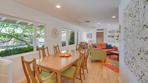 A modern dining area with a wooden table and chairs, a sofa, and a bookshelf. - Patio, Pool & Mountain Views: Palm Springs Home! (Palm Springs)