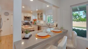 A modern kitchen with white cabinetry, a central island, and a view of greenery outside. - Patio, Pool & Mountain Views: Palm Springs Home! (Palm Springs)